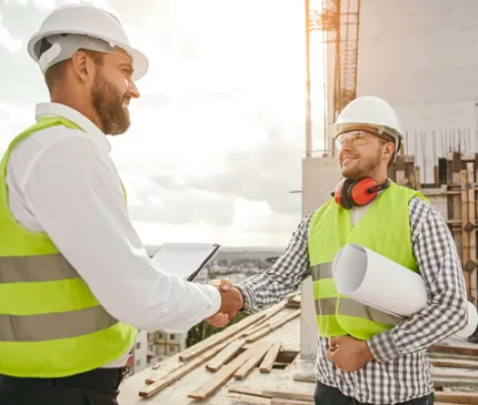 two construction workers wearing yellow vests shaking hands