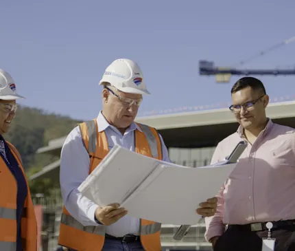 Besix Watpac Project Manager And Indigenous Employee Showing Plans To NAIF Staff With JCU Engineering And Innovation Place Construction Site And Crane In Background