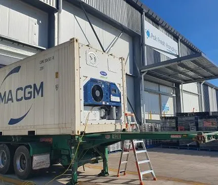 view of the loading dock of the cold storage facility which is made of steel and corrugated iron sheets with the back of a truck loading product into the facility